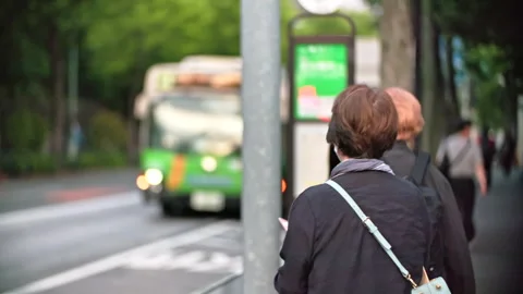 Japanese bus making stop at bus stop in Tokyo with passenger waiting to ride the Stock Footage 244052503