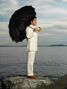 Japanese businessman holding umbrella near ocean Stock Photos