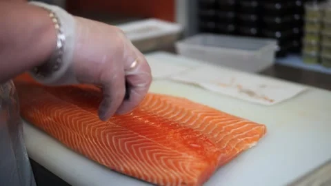A Japanese chef in gloves carefully pulls bones from a large salmon with tongs T Stock Footage 284701970