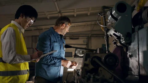 Japanese engineer controlling mature worker indoors in metal workshop. Stock Footage 164537585