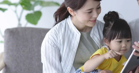 Japanese kid using tablet on the sofa with her parents Видео 94319067