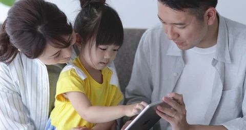 Japanese kid using tablet on the sofa with her parents Видео 94319078