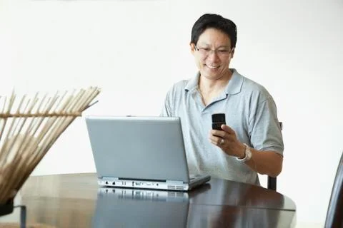 Japanese man using laptop and checking cell phone at table Stock Photos