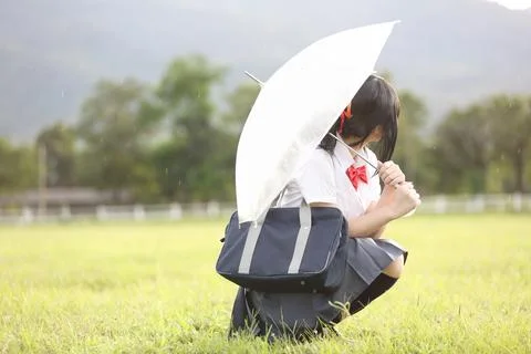 Japanese school with umbrella on rain in countryside with grass mountain an.. Stock Photos