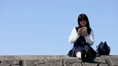 Japanese Schoolgirl Using Smartphone While Sitting Under Blue Sky Stock-Footage 344236567