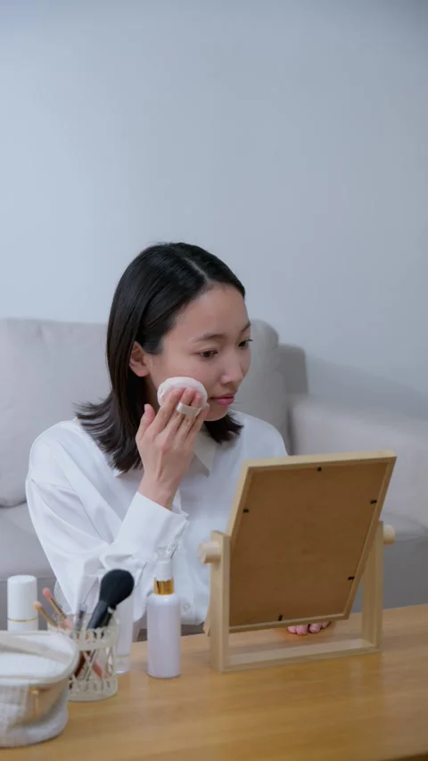 Japanese woman applying makeup while looking in the mirror in the living room Stock Footage 336767660