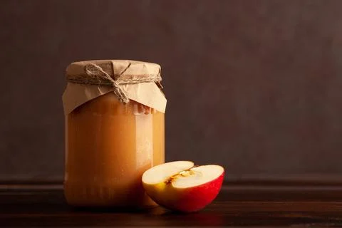 Jar of apple jam with apple slice on dark wooden table. Space for text Stock Photos