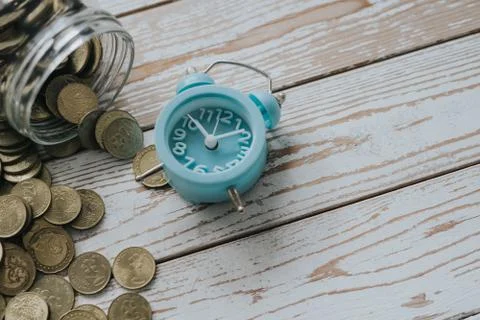Jar of coins with analog alarm clock on vintage wooden table.Financial and in Stock Photos