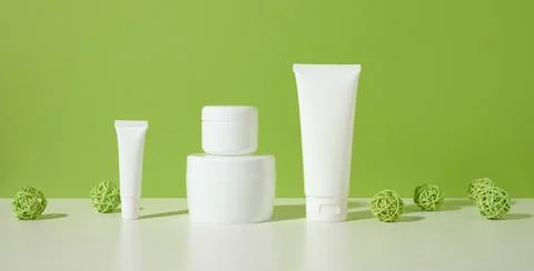 Jar, empty white plastic tubes for cosmetics on a white table, green backgrou Stock Photos