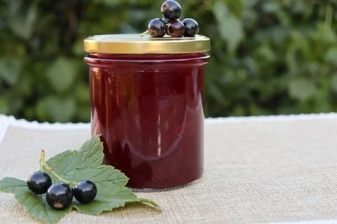Jar of fruit jam with blackcurrants on a table outside in day time Stock Photos