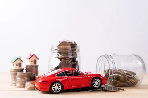 Jar full of coins with stack coin and red car on wooden table isolated grey b Stock Photos