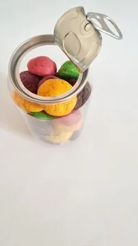 Jar with metal pull-tab lid containing colorful cookies on a white background Stock Photos