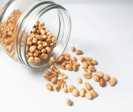 A jar of peanuts is opened and spread out and isolated on a white backgroun.. Stock Photos