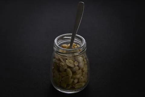 Jar of peanuts with spoon on dark background creative food image Stock-Fotos