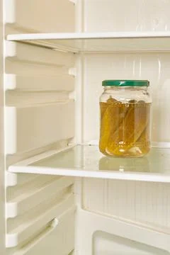 Jar of pickled cucumbers is on the shelf of an empty refrigerator Stock Photos