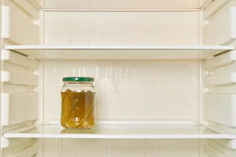 Jar of pickled cucumbers is on the shelf of an empty refrigerator Stock Photos