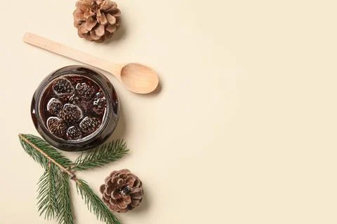 Jar of tasty pine cone jam with spoon and fir tree branch on beige background Stock Photos