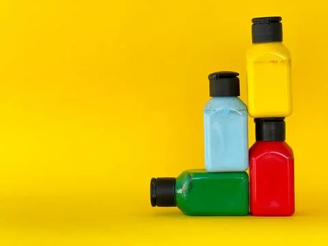 Jars with bright multi-colored acrylic paint on a yellow background. Still life Stock Photos