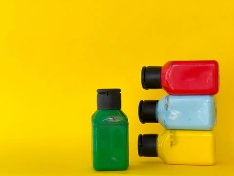 Jars with bright multi-colored acrylic paint on a yellow background Stock Photos