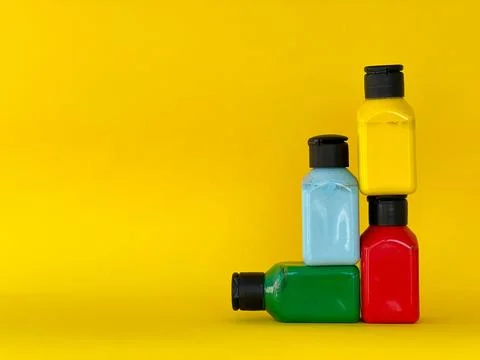 Jars with bright multi-colored acrylic paint on a yellow background Stock Photos