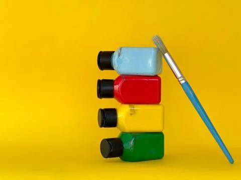 Jars with bright multi-colored acrylic paint and brush on a yellow background Foto stock