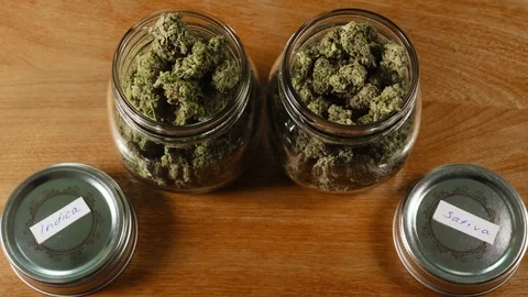 Jars of cannabis on wood table lids off labeled 스톡 동영상 94339034