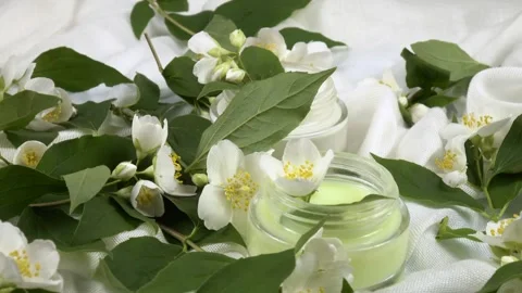 Jars with face cream, fresh flowers philadelphus are on a white background Stock Footage 335881087