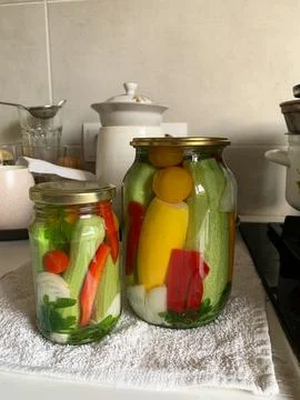 Jars filled with cucumbers, peppers, and zucchini sit on a wooden countertop. Stock Photos