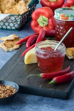 Jars of hot pepper jelly surrounded by peppers, cracker bread and cheese. Stock Photos