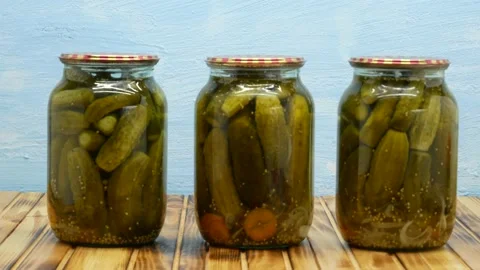 Jars with pickled cucumbers are placed on a wooden table on a blue background. Stock Footage 204146652