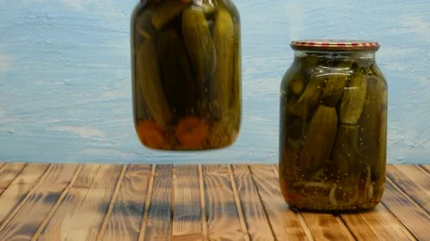 Jars with pickled cucumbers are placed on a wooden table on a blue background. Stock Footage 205722119