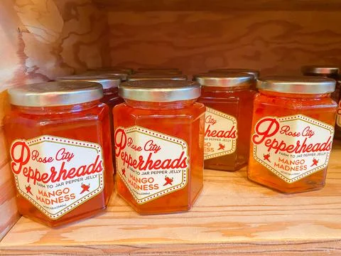 Jars of Rose City Pepperheads Mango Madness pepper jelly on a wooden shelf .. Photos