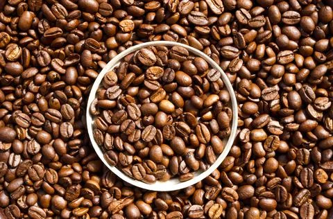 Java. Roasted coffee beans in a paper cup lid against the background of beans Stock Photos