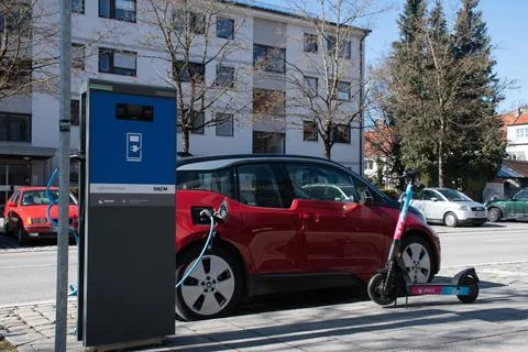 Jawls Shared E-Scooter Parked next to BMW i3 Electric Car at Charging Station Stock Photos