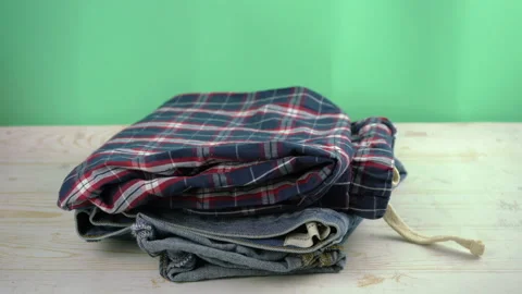 Jeans, pajama, shirts falling on the table in a stack Stock Footage 125402129