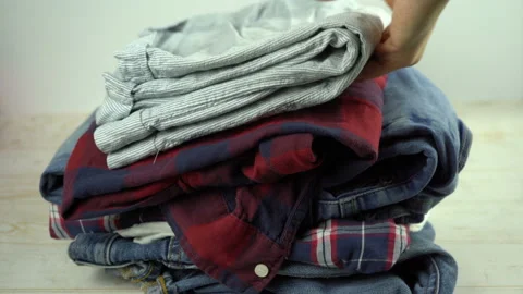Jeans, pajama, shirts falling on the table in a stack. Clothes for donation Stock Footage 135582195
