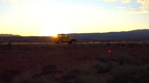 Jeep driving along the dirt road through the desert at gorgeous morning sunrise Stock Footage
