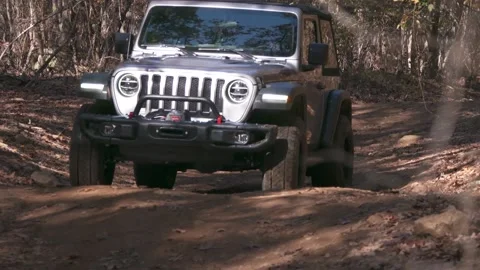 JEEP MAKES ITS WAY DOWN A TRAIL AND CRAWLS OVER A ROCK IN THE WOODS Stock Footage 136123975