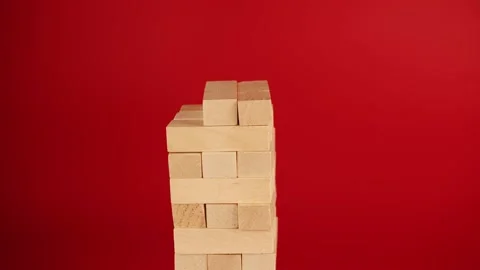 Jenga game on red background. Woman's hand builds tower of small wooden blocks Video stock 197533795