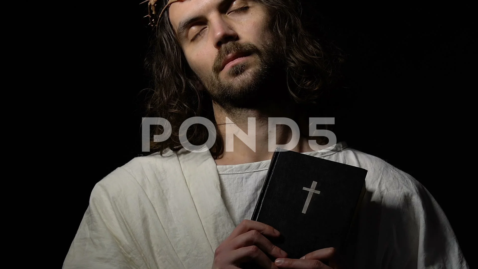 Jesus Christ with eyes closed in crown of thorns holding bible crucifixion