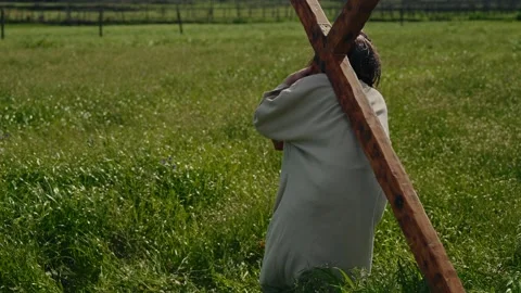Jesus Christ kneeling in grass picking up wooden cross onto his shoulder 库存影片 333095910