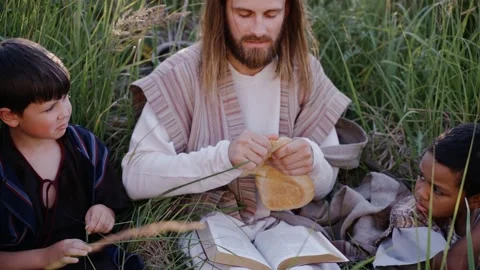 Jesus gives bread to children while sitting among the grass on the hill. Stock Footage 160496802
