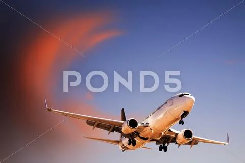Jet aeroplane landing from bright twilight sunset sky Stock Photos
