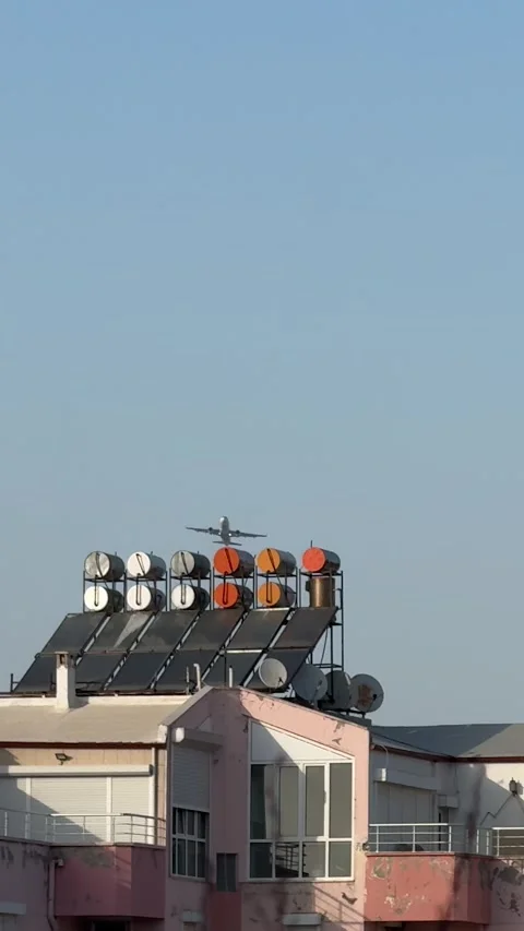 A jet airplane taking off, emerging from behind the rooftops of buildings aga Stock Footage 303360073