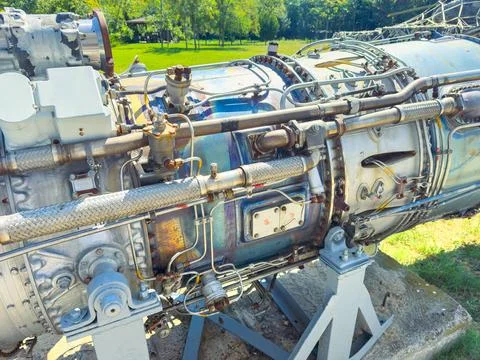 A jet engine rests on a stand in a park. The shiny metal parts reflect the su Stock Photos