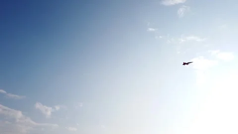 Jet plane flying across clear blue sky with scattered clouds, aerial view. Stock Footage 337388214