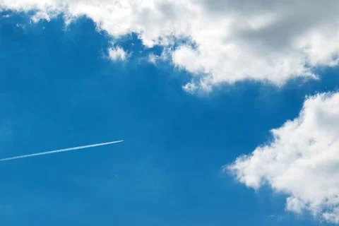 Jet plane high in the clouds, trail from the plane in the blue sky Stock Photos