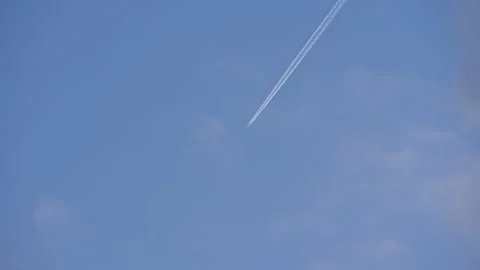 A jet plane soars through a vast blue sky, leaving a crisp white contrail in its Stock Footage 312173604