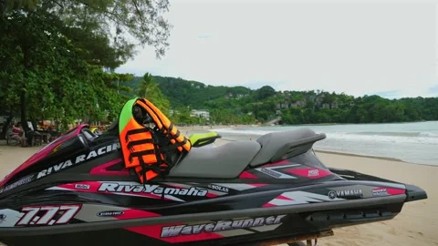 Jet ski with life jackets placed on sandy beach with lush green hills Stock Footage 277618084