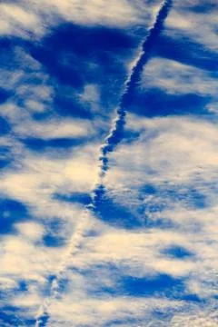 Jet stream running through white clouds in a blue sky Stock Photos